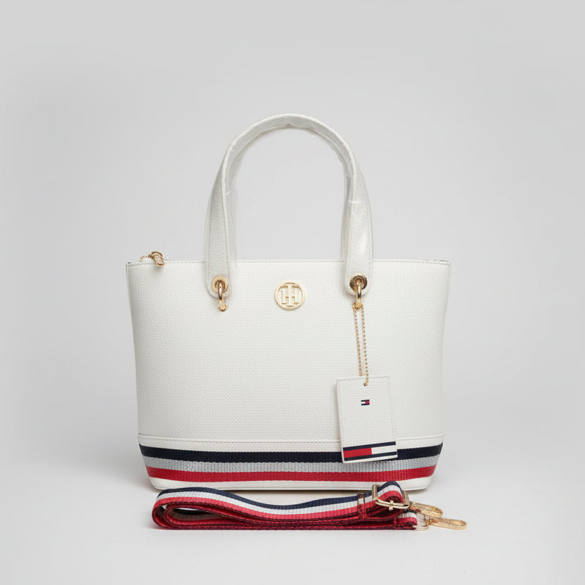 White handbag with a strap and tag on a light surface with a textured white wall background