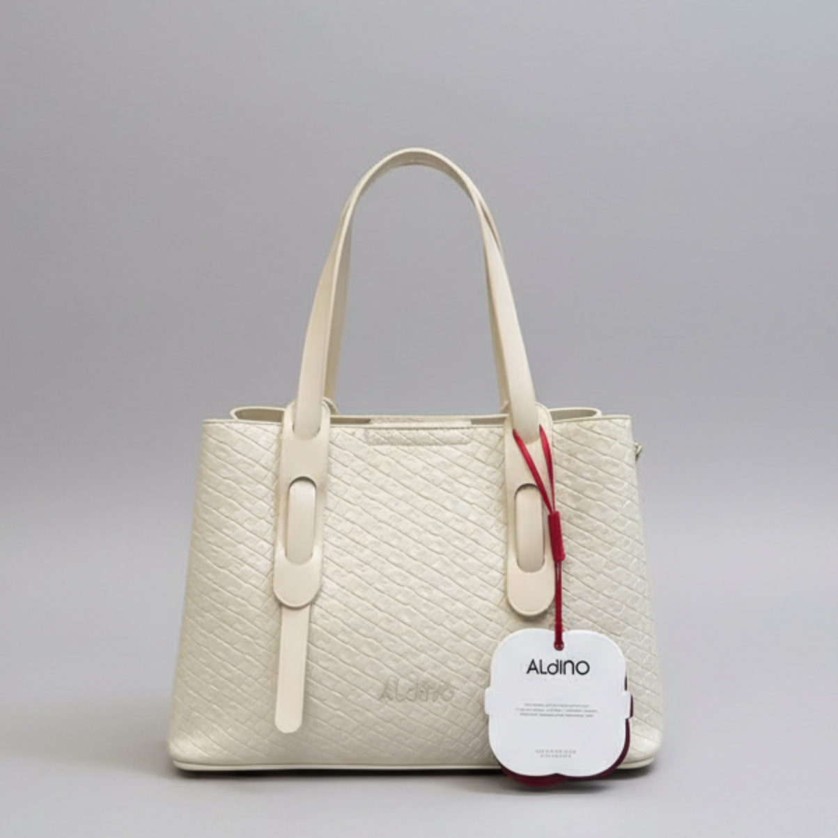 An off-white textured leather handbag with double top handles and a hanging white brand tag, photographed against a neutral gray studio background.