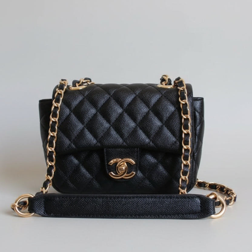 Black quilted handbag with gold chain and clasp on a light surface with white tiled wall background