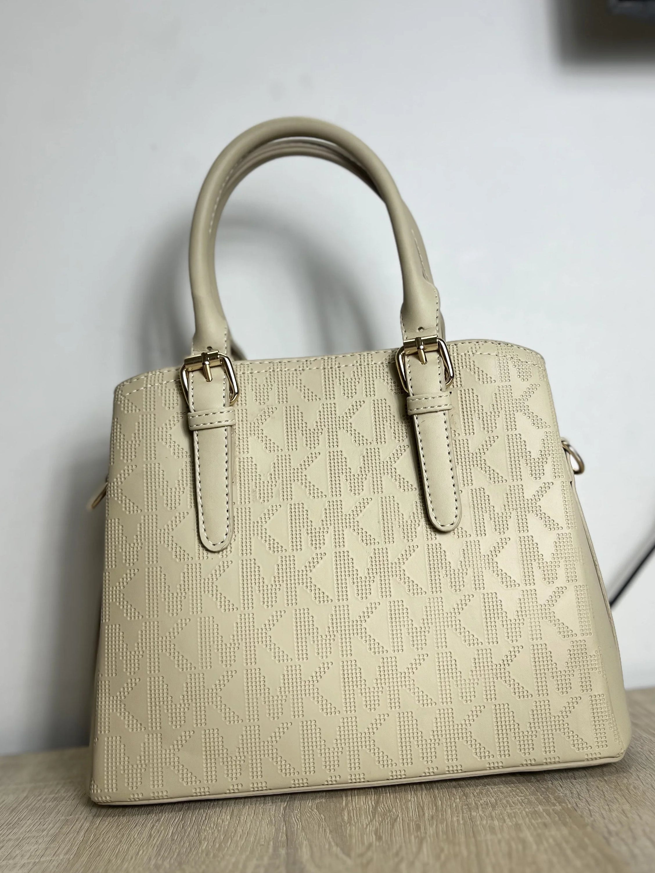 Beige handbag on a wooden surface with a light gray wall in the background